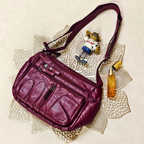 Purple handbag on a decorative doily with a small figurine and bottle of perfume.
