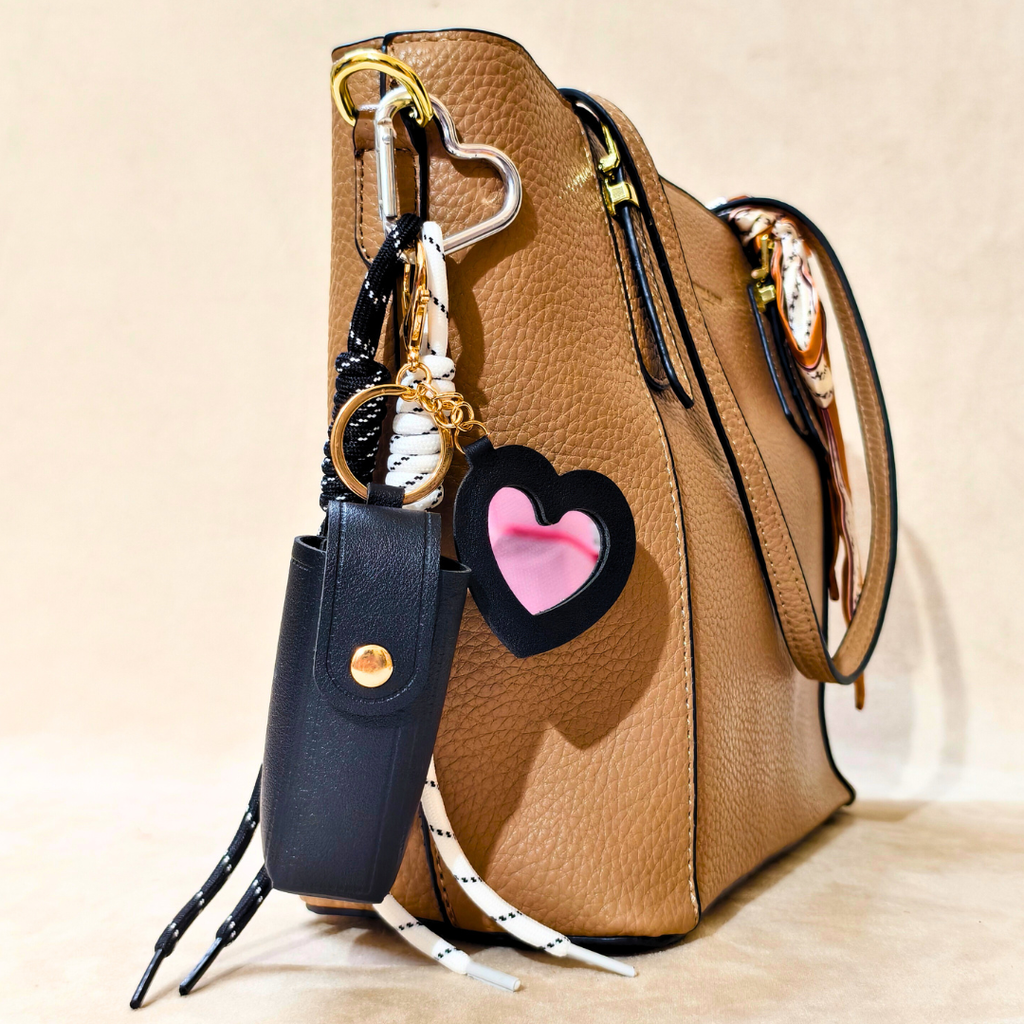 Brown leather handbag with a black keychain and heart-shaped charm on a beige background