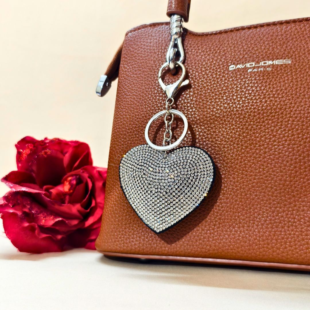 White Heart Keychain with a metal latch placed on a purse beside a flower decoration in front of a beige background