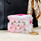 Small pink and white embellished pouch with a keychain on a neutral background