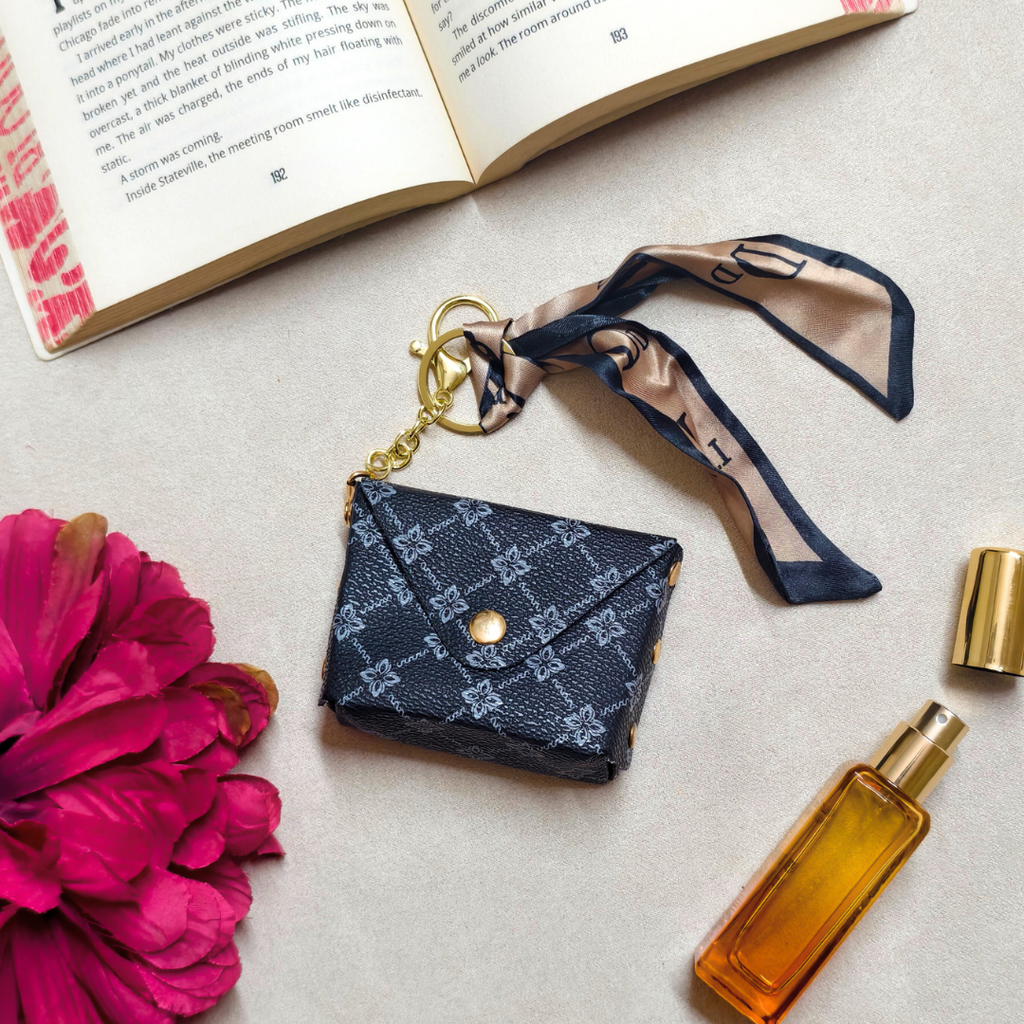 Small blue patterned purse with a keychain, pink flower, and perfume bottle on a light surface.