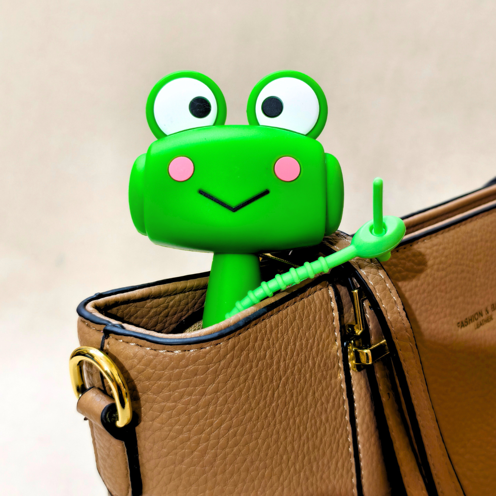A bright green frog-shaped zipper pull designed to keep bags closed, shown attached to a brown textured leather handbag.