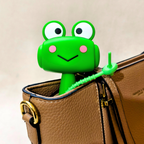 A bright green frog-shaped zipper pull designed to keep bags closed, shown attached to a brown textured leather handbag.