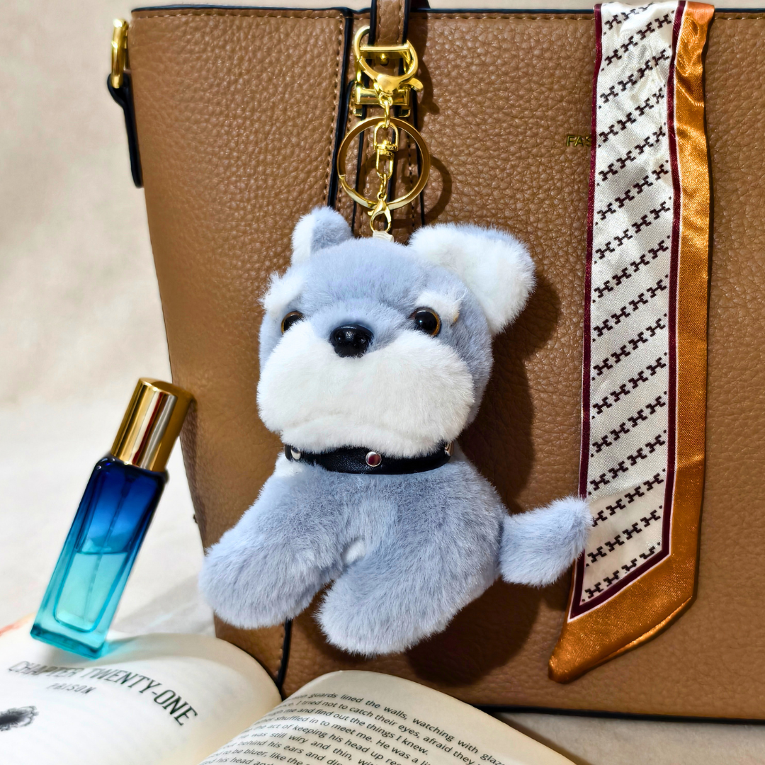 Fluffy dog-shaped keychain on a brown leather bag with a blue perfume bottle and open book.