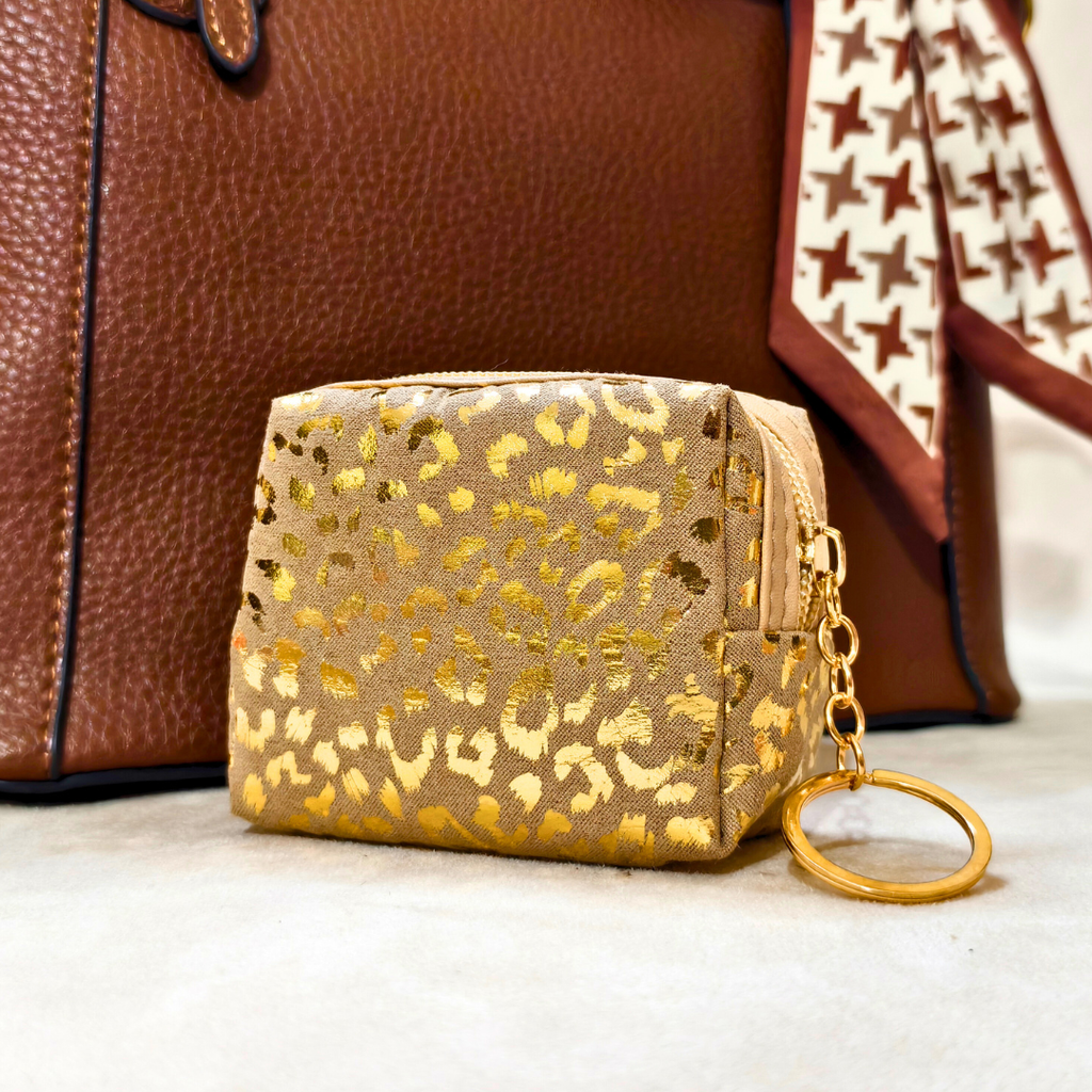 Small pouch with gold leopard print and keychain attachment in front of a brown leather bag.