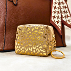 Small pouch with gold leopard print and keychain attachment in front of a brown leather bag.