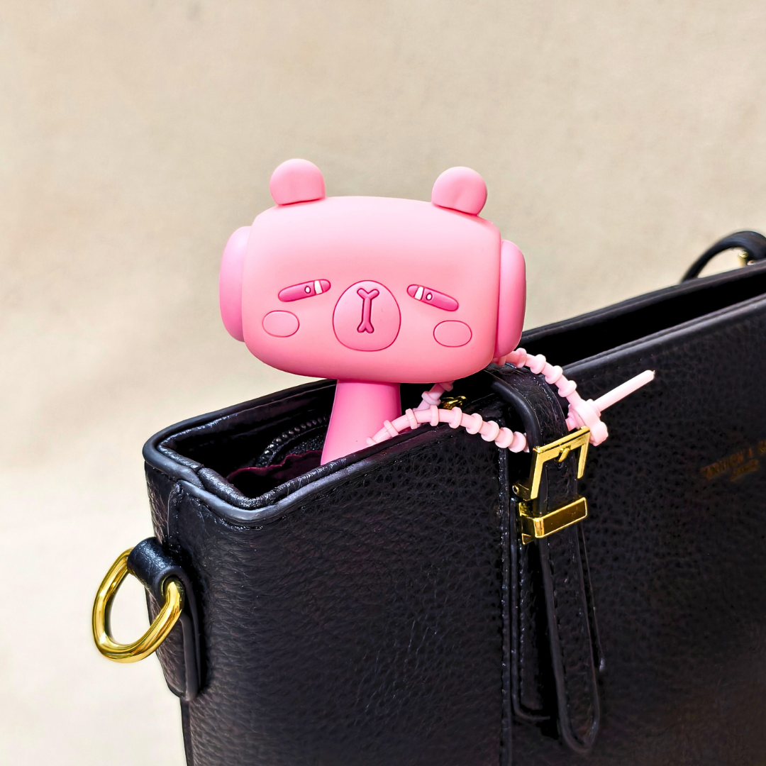 Pink cartoon character keychain attached to a black handbag with a beige background