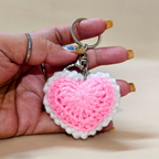 Hand holding a pink and white heart-shaped keychain against a beige background