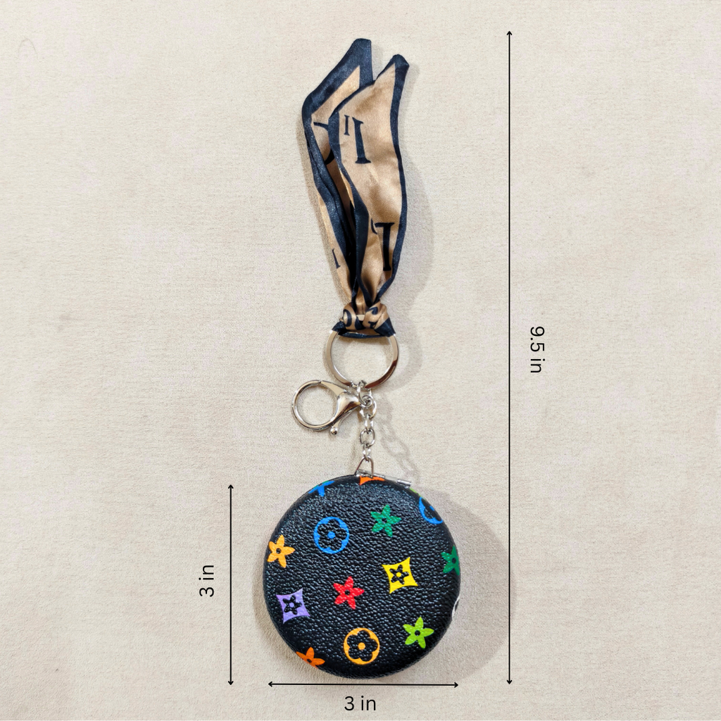 A small round black monogram keychain bag with a matching neck strap, shown on a light beige background with dimension lines indicating a height of 9.5 inches and a width of 3 inches.