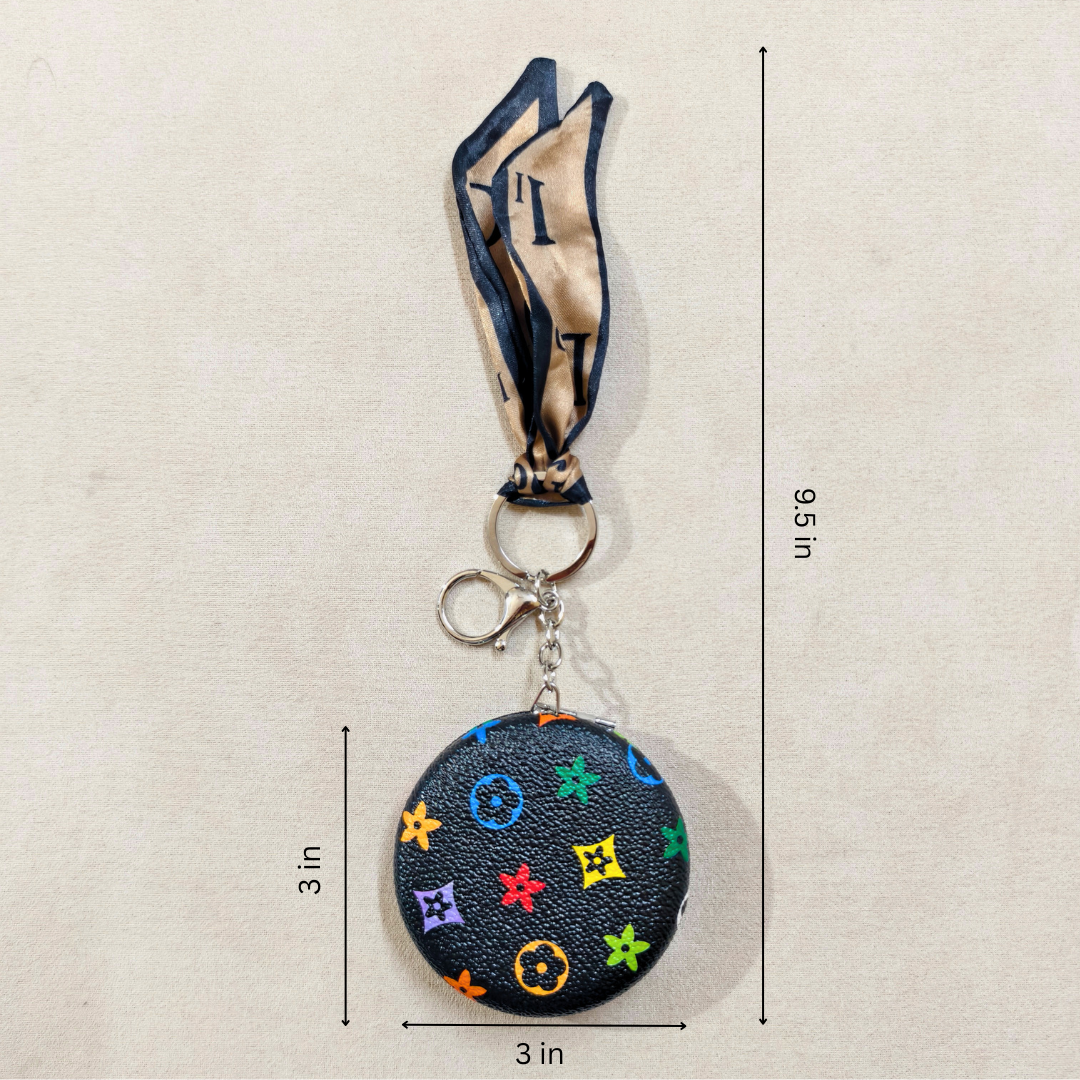 A small round black monogram keychain bag with a matching neck strap, shown on a light beige background with dimension lines indicating a height of 9.5 inches and a width of 3 inches.