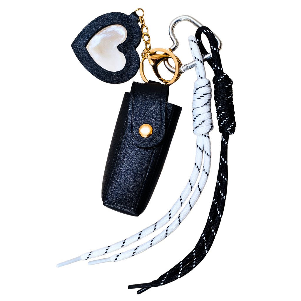 Black leather keychain pouch with heart-shaped cover, white and black braided lanyard, and gold ring on a white background.