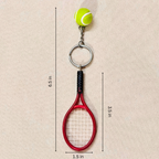 A novelty tennis racket keychain featuring a red tennis racket head with white strings, a black wrapped grip, a silver split ring, a short chain, and a small yellow-green tennis ball charm with white lines, shown on a beige background with measurements.