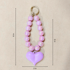 Pink beaded keychain with a purple heart pendant on a beige background
