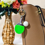 Sporty Table tennis Keyring Attached with silver chain and ring along with white ball attached on Hand bag as bag charm on beige background.