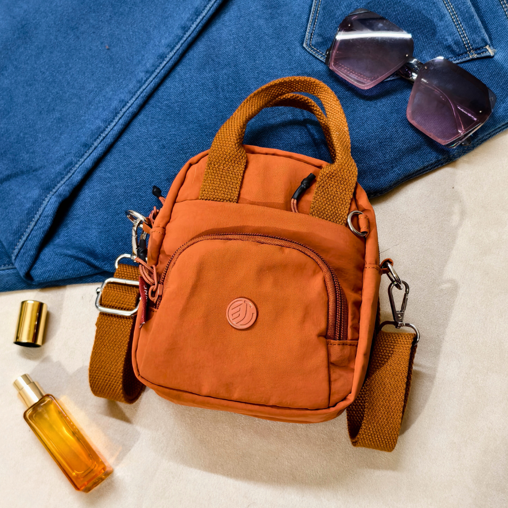 Orange handbag with sunglasses and a bottle on a blue fabric background
