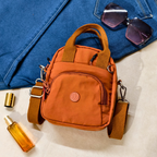 Orange handbag with sunglasses and a bottle on a blue fabric background