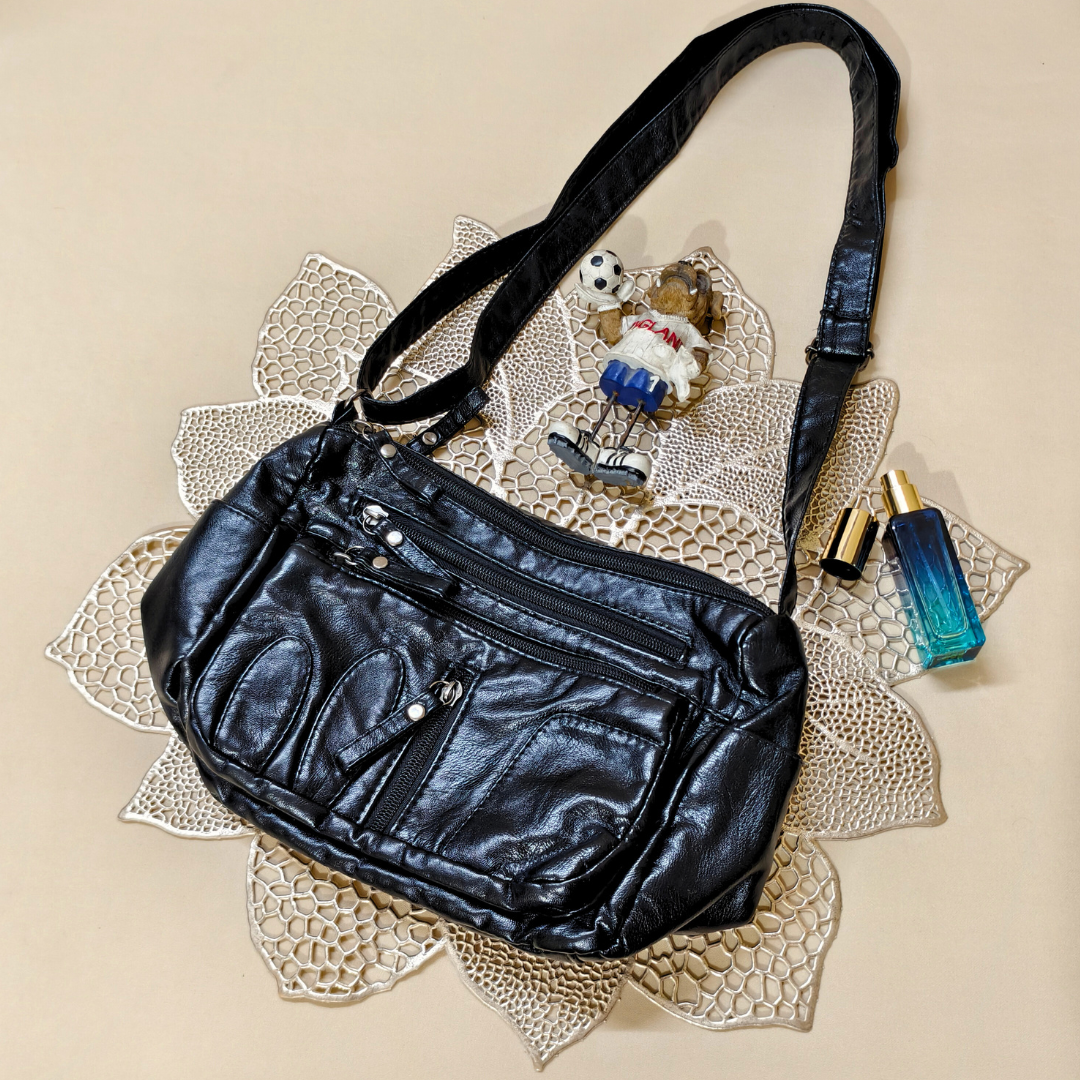 Black leather handbag on a decorative doily with a teddy bear and perfume bottle.