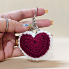 Hand holding a crocheted heart keychain with a beige background
