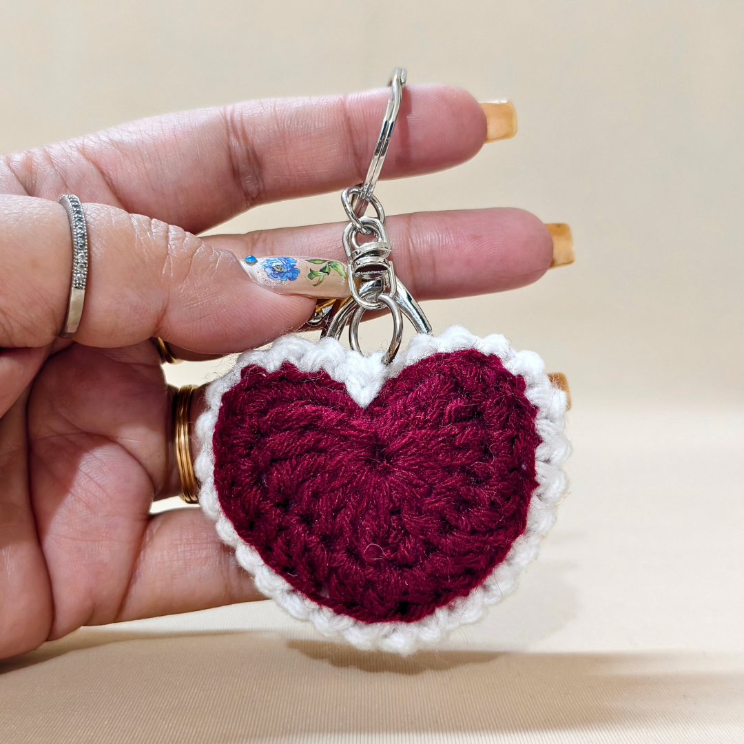 Hand holding a crocheted heart keychain with a beige background