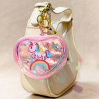 Heart-shaped keychain with a unicorn design on a beige bag.