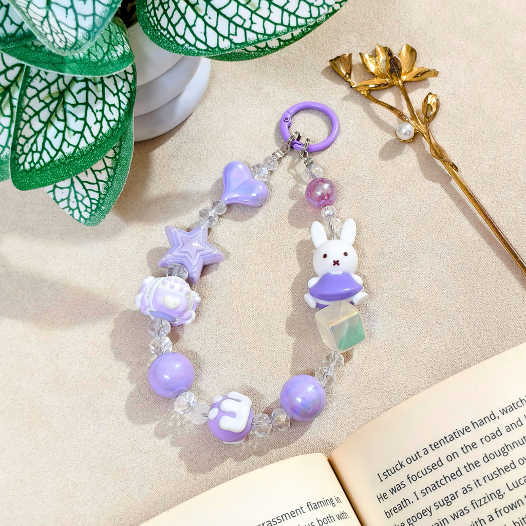 Purple beaded keychain with a bunny charm on a beige surface with a book and decorative elements.