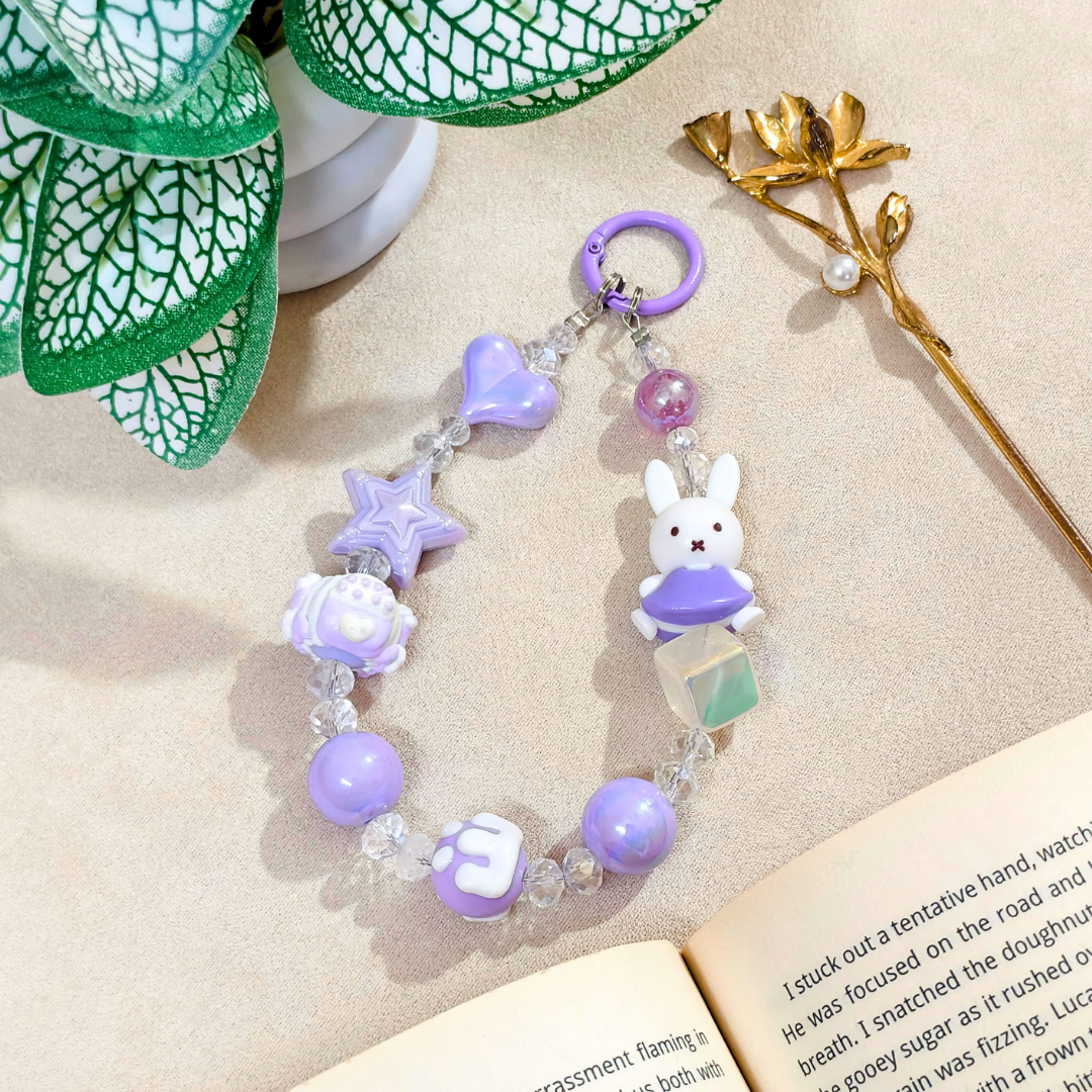Purple beaded keychain with a bunny charm on a beige surface with a book and decorative elements.