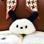 Fluffy white ghost keychain with black eyes and ears on an open book