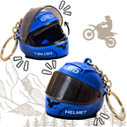 Two blue motorcycle helmet keychains with gold split rings, shown on a white background with decorative line drawings of mountains, trees, and a motorcycle silhouette.
