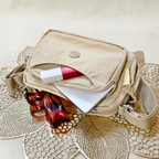 Khaki Beige Sling Bag With Items In Front Of Beige Background.