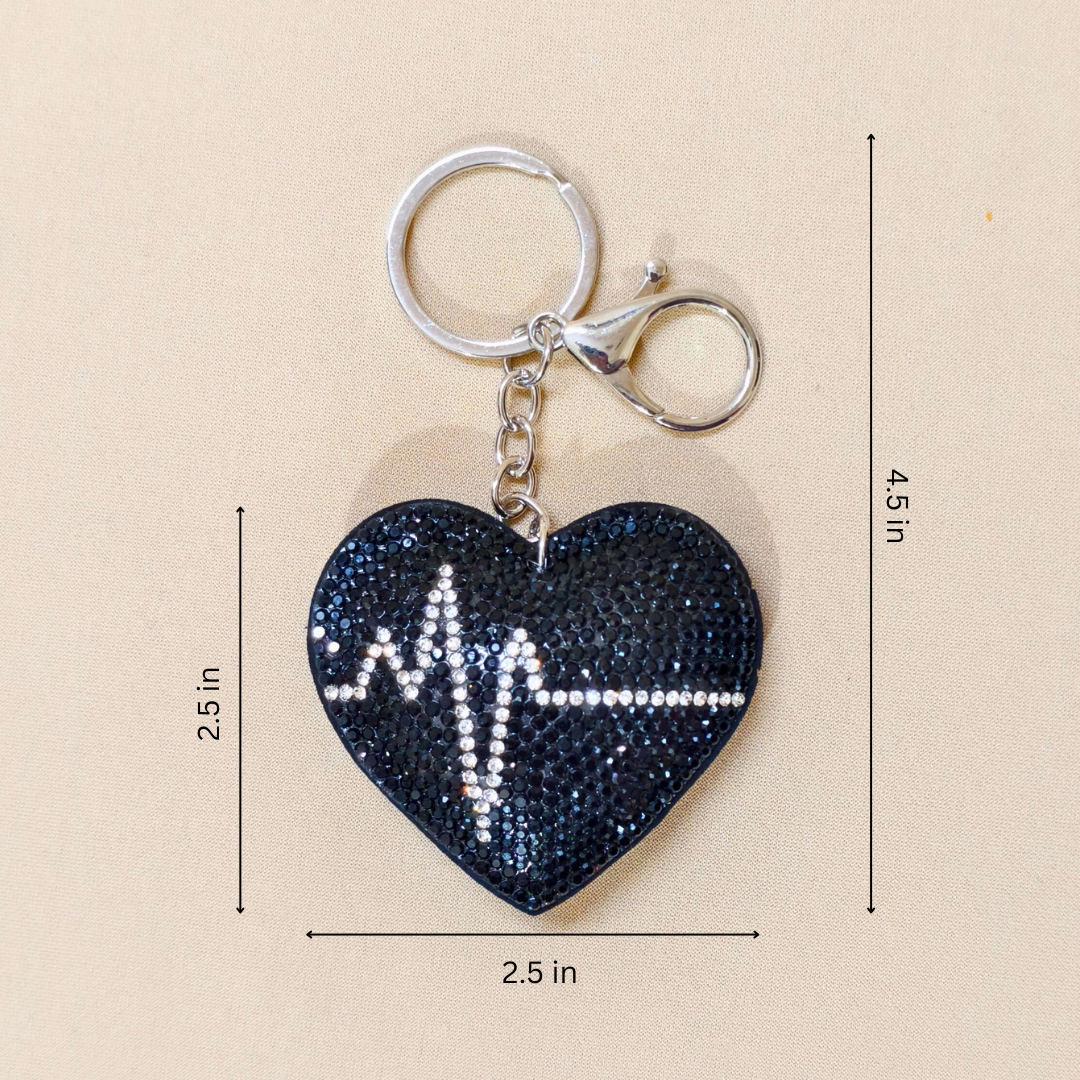 Black heart keychain with a metal latch in front of a beige background with measurements