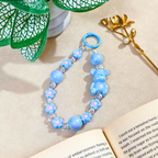 Blue beaded bracelet with teddy bear and flower designs on a beige surface with a book and decorative elements.