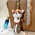Plush animal keychain attached to a brown leather bag with a blue perfume bottle and open book in the foreground.