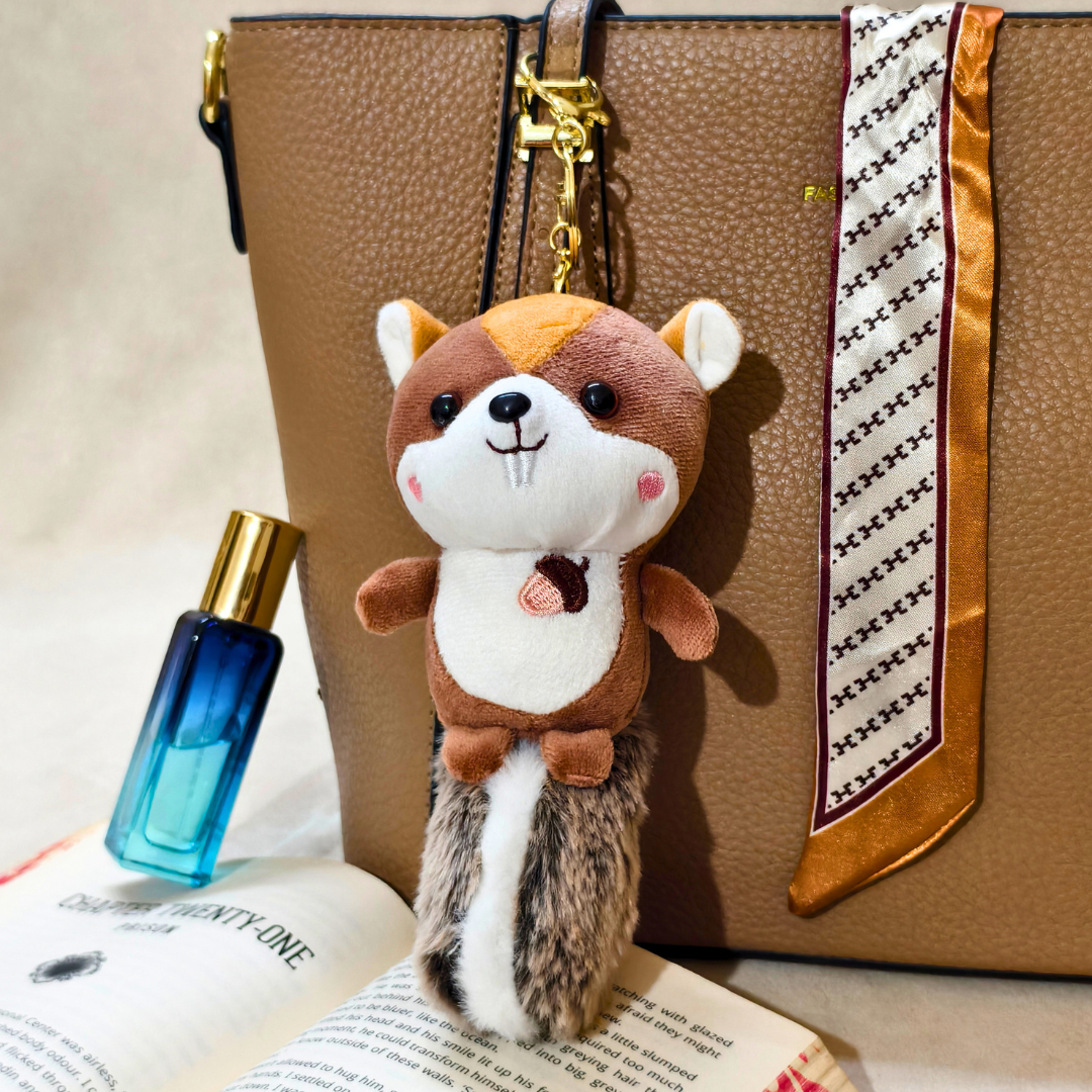 Plush animal keychain attached to a brown leather bag with a blue perfume bottle and open book in the foreground.