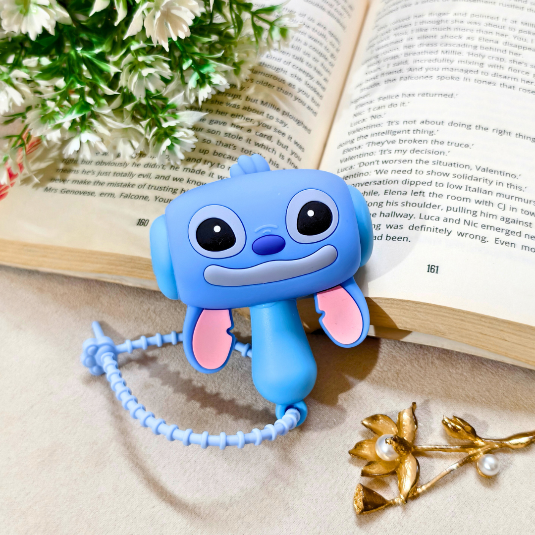 Blue cartoon character with a pink bow on an open book with flowers and a gold flower arrangement.