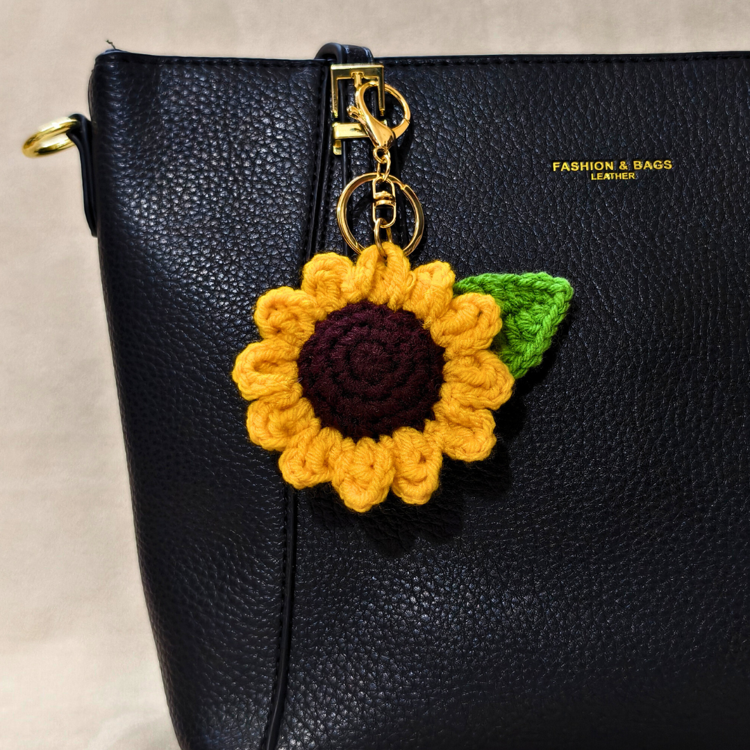 Black leather handbag with a yellow sunflower keychain on a neutral background