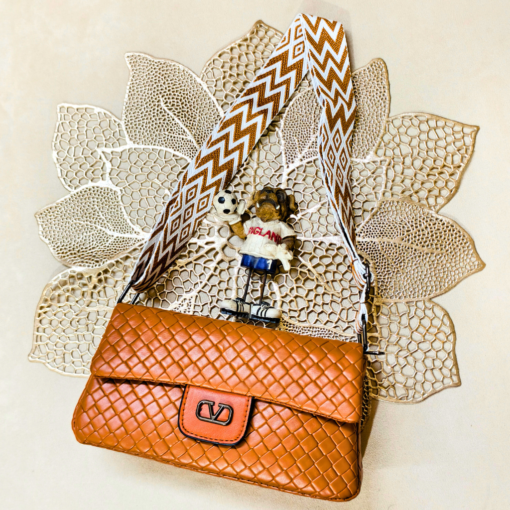 Brown woven handbag with a decorative strap on a textured beige background