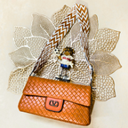 Brown woven handbag with a decorative strap on a textured beige background