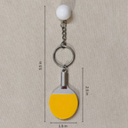 A miniature table tennis keychain charm, featuring a yellow and black paddle with a small white ball and silver metal key ring showing measurement.