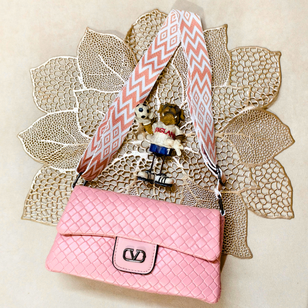 Pink handbag with a decorative strap on a textured beige background
