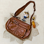Brown leather bag with a strap, small figurine, and bottle on a textured surface