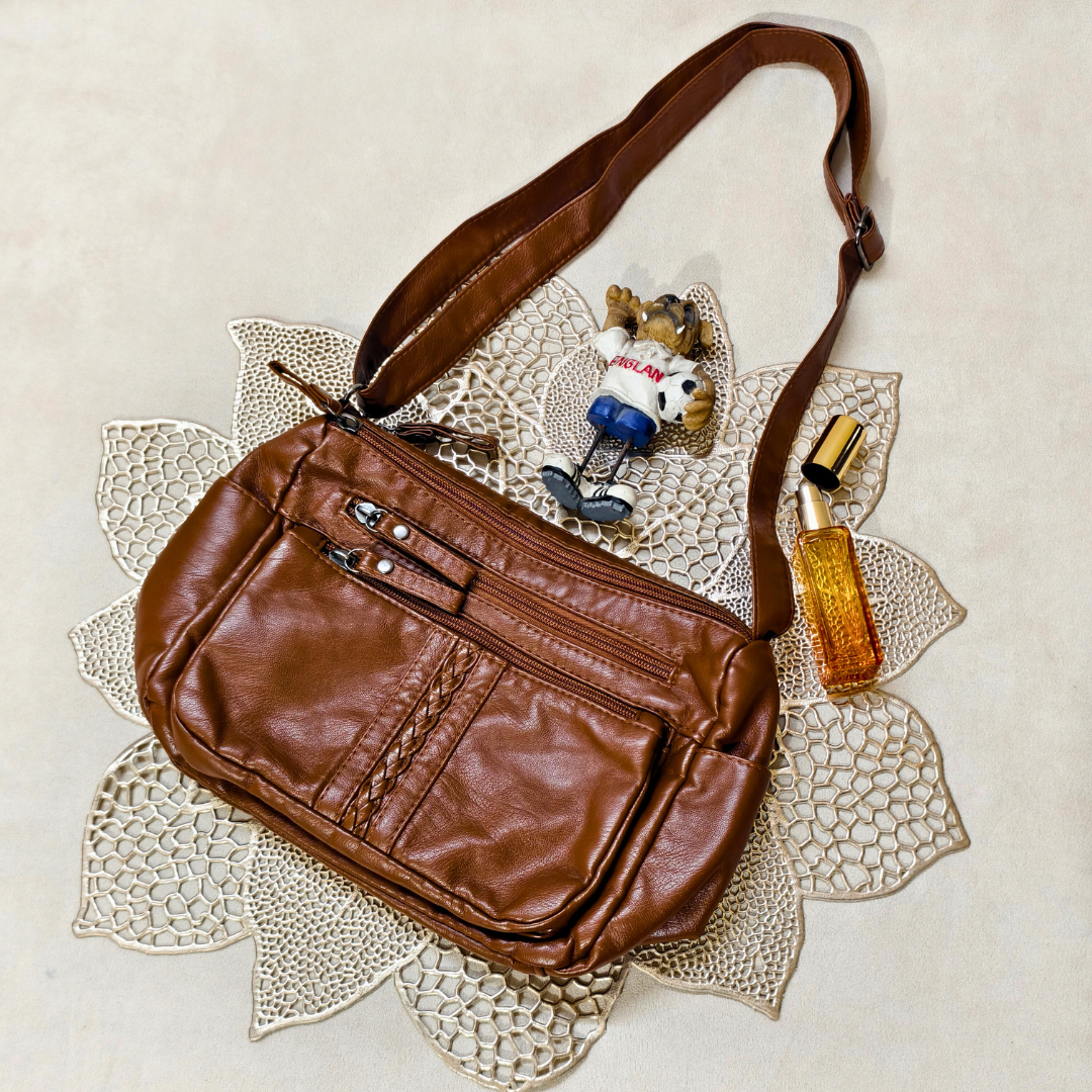 Brown leather bag with a strap, small figurine, and bottle on a textured surface