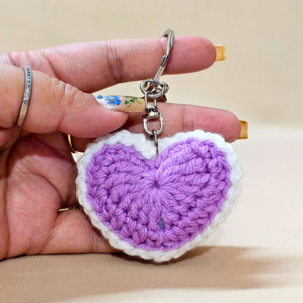 Hand holding a purple heart-shaped keychain against a beige background