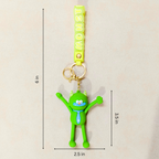 A green cartoon monster keychain with a yellow strap printed with 'UNSWISS' and gold keyring hardware, shown on a light beige background with measurement lines and labels indicating 6 in height, 3.5 in width, and 2.