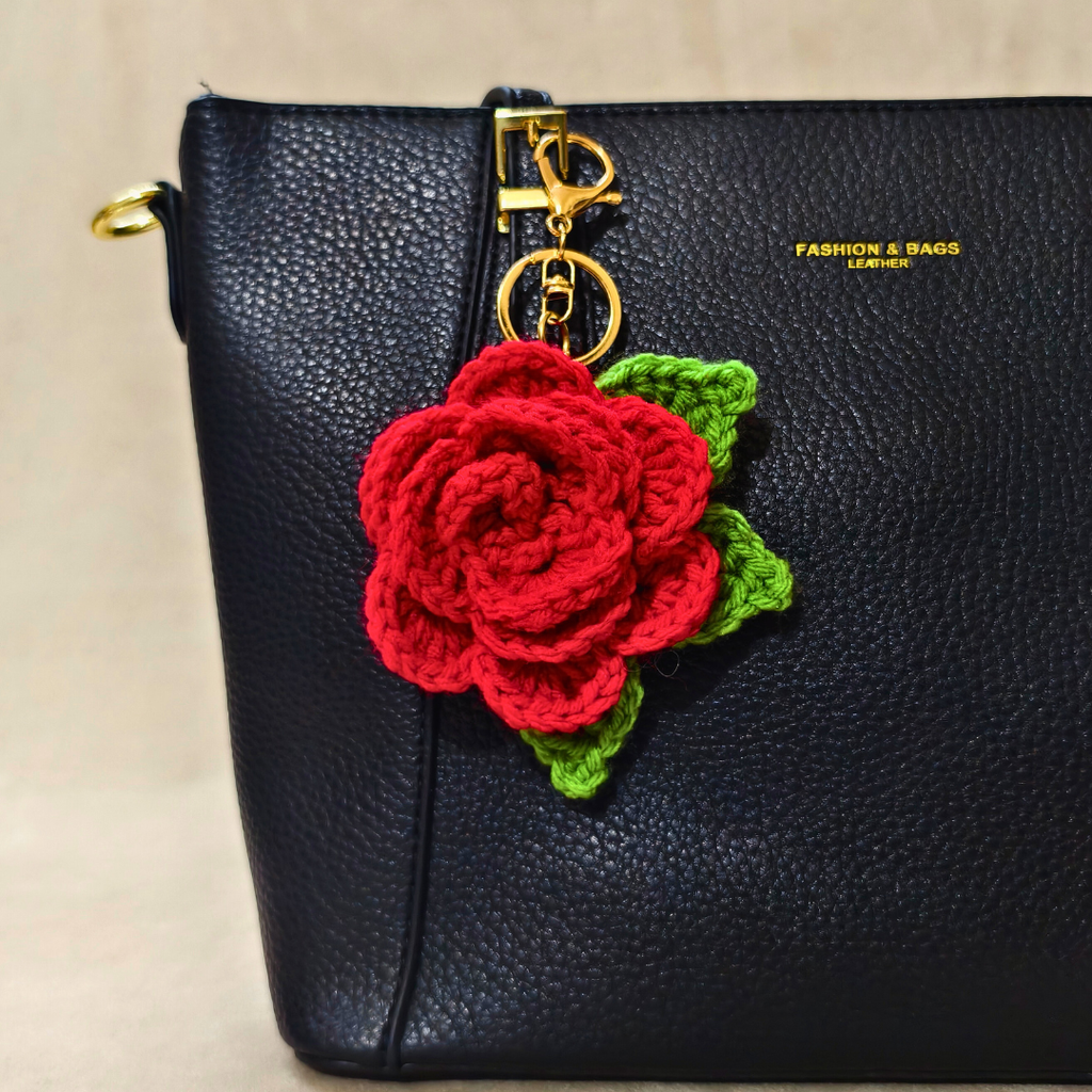 Black handbag with a red crocheted rose keychain on a beige background