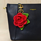 Black handbag with a red crocheted rose keychain on a beige background