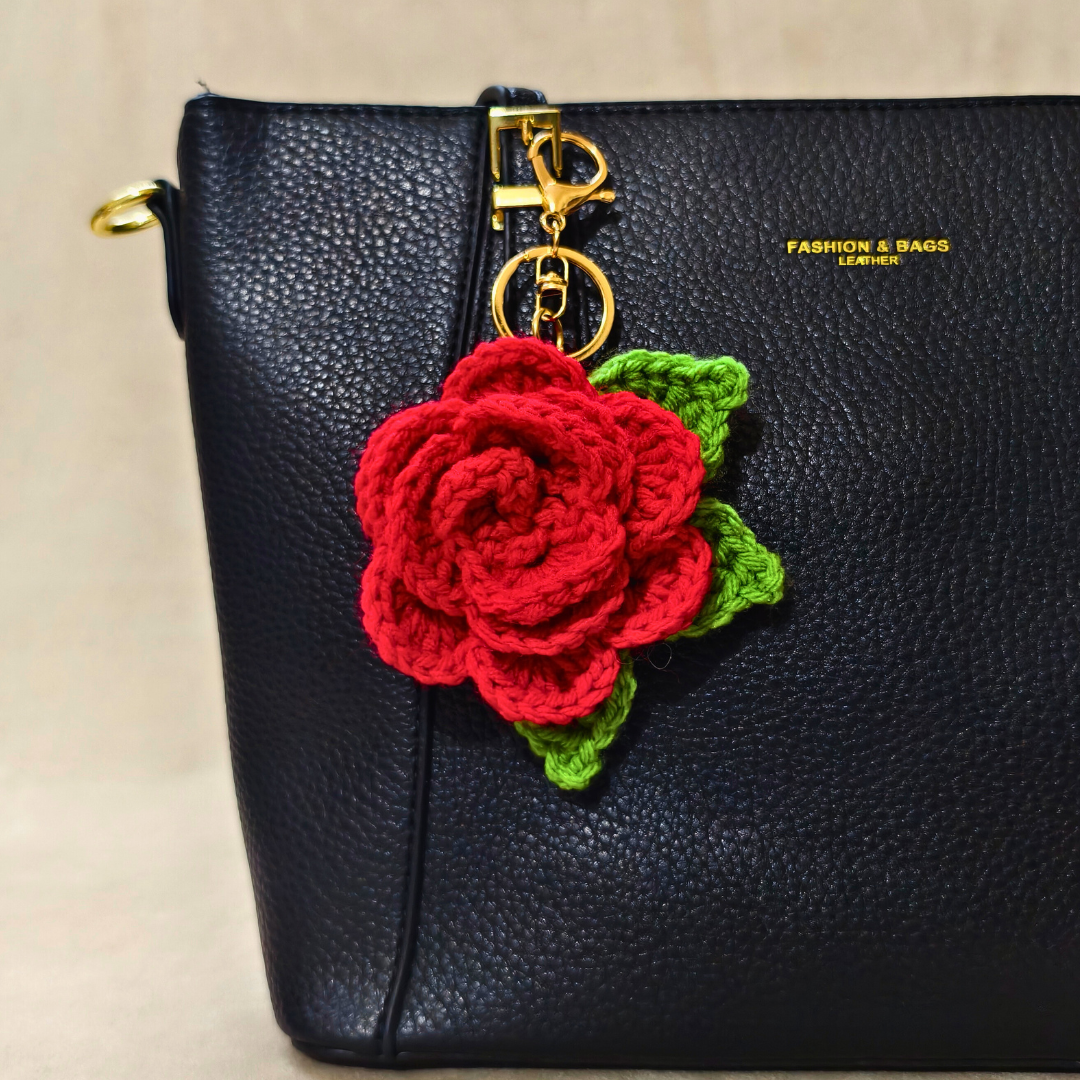 Black handbag with a red crocheted rose keychain on a beige background