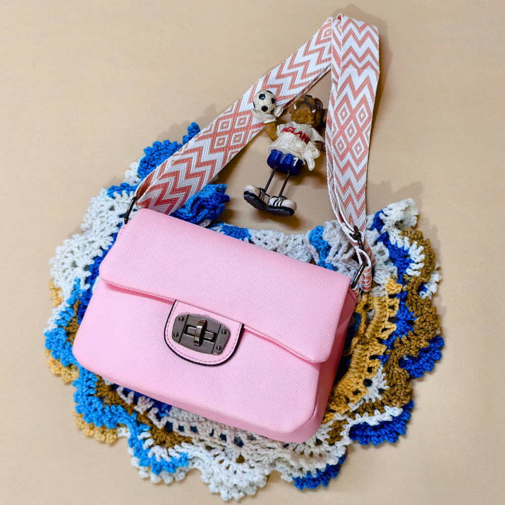 Pink handbag with a patterned strap on a textured surface