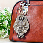 Keychain with owl design on a brown leather bag with a blurred floral background