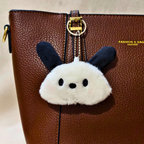 Fluffy keychain with black ears attached to a brown leather bag.