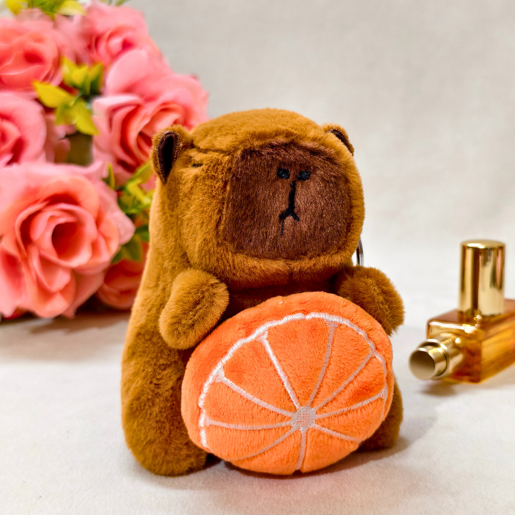 Brown teddy bear with an orange and a gold bottle on a white surface with pink flowers in the background